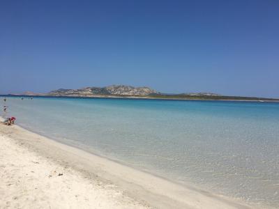 Spiaggia con sabbia bianca, mare cristallino e montagne sullo sfondo.