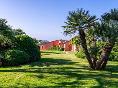 Casa rossa con giardino verde e palme sotto cielo azzurro.