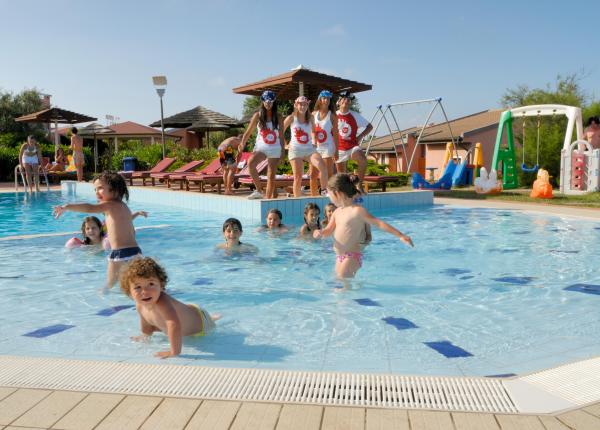 Bambini che giocano in piscina con animatori in un resort.