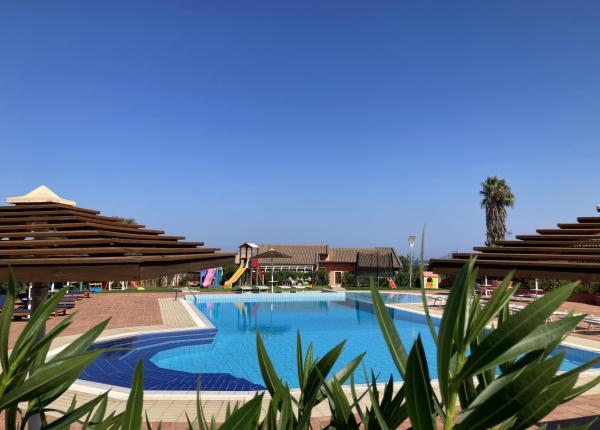 Piscina con ombrelloni, cielo sereno e palme.