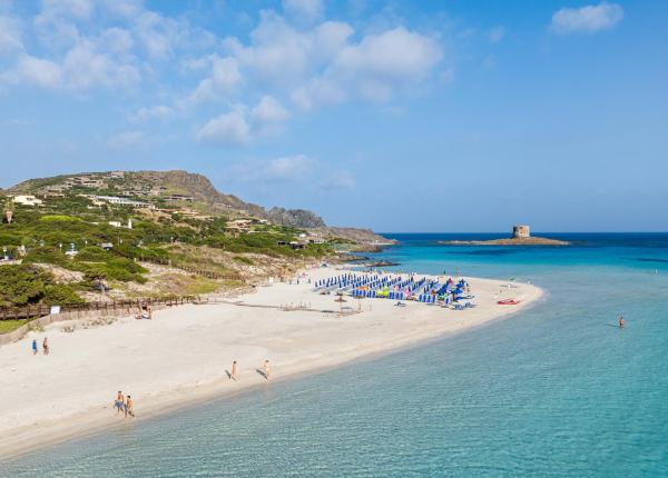 Spiaggia sabbiosa con mare turchese e torre in lontananza.