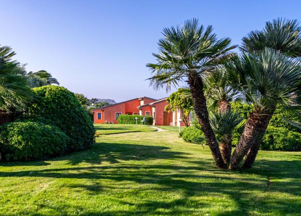 Casa rossa con giardino verde e palme sotto cielo azzurro.