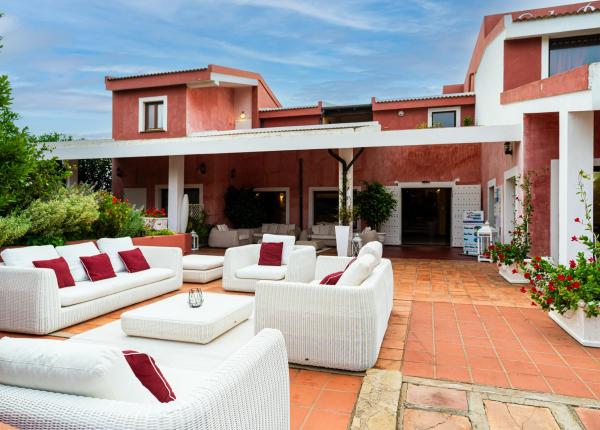 Elegante terrazza con divani bianchi, cuscini rossi e piante fiorite.
