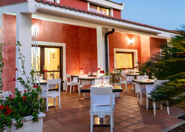 Ristorante all'aperto, atmosfera romantica, luci soffuse, sedie bianche, piante verdi.