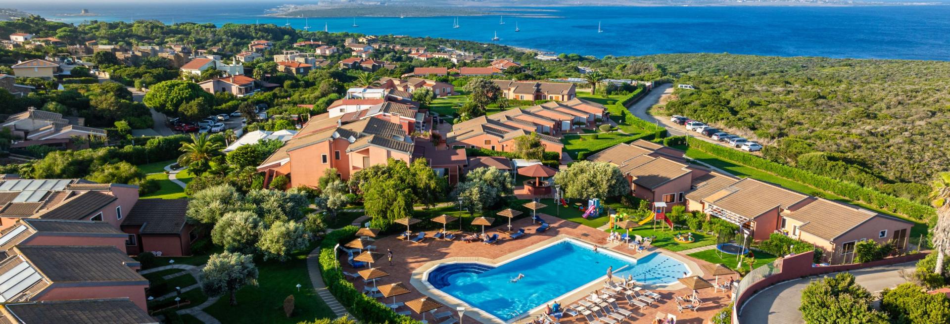Vista aerea di un villaggio con piscina e mare azzurro sullo sfondo.