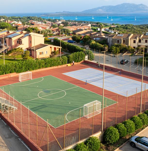 Campo sportivo vicino al mare, case colorate e natura rigogliosa.